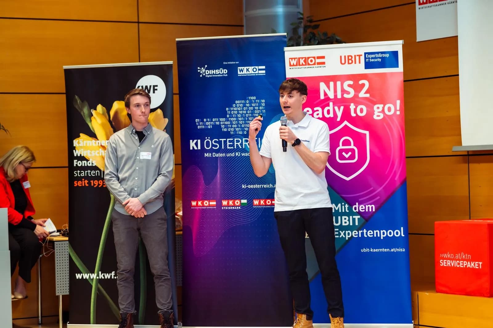 Vortragssituation beim WKO Business-Frühstück: Sprecher mit Mikrofon vor Roll-ups von DIH Süd/KI Österreich und der UBIT („NIS 2 – Ready to go“)