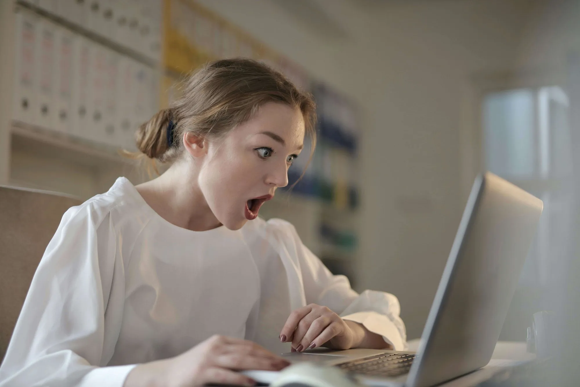 Symbolbild: Eine Frau im Büro blickt schockiert auf ihren Laptop.